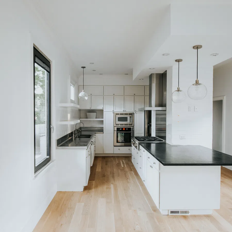 Bright modern kitchen with white cabinetry, black countertops, hardwood floors, and pendant lighting over island.