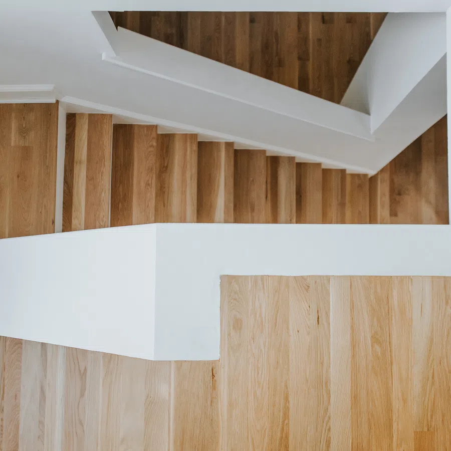 Top view of a modern wooden staircase with white railings in a minimalist interior space.