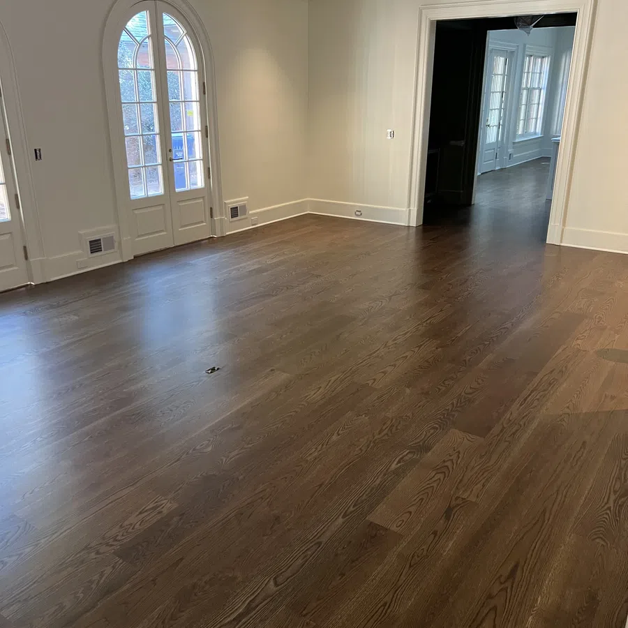 Empty room with dark hardwood floors, cream walls, arched glass doors, and an open doorway to a sunlit space.