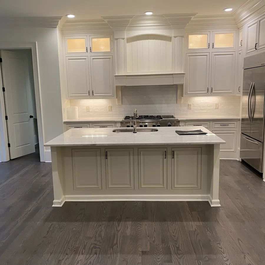 Modern kitchen with white cabinets, marble island, stainless steel appliances, and dark hardwood floors.