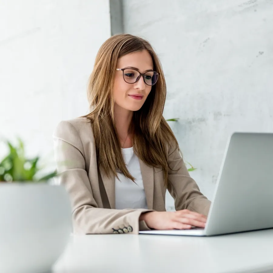 Professional woman working on a laptop at a modern office desk with plants.