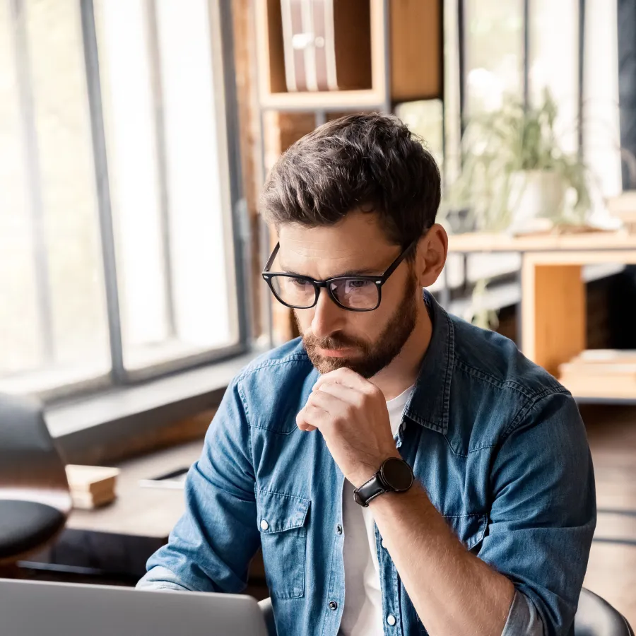 Focused man working on a laptop in a modern office environment with natural light.
