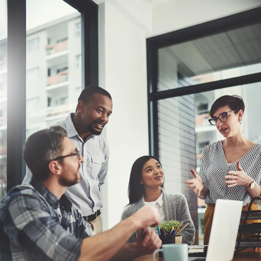 A diverse team collaborates around a laptop in an office setting, discussing ideas and strategies.