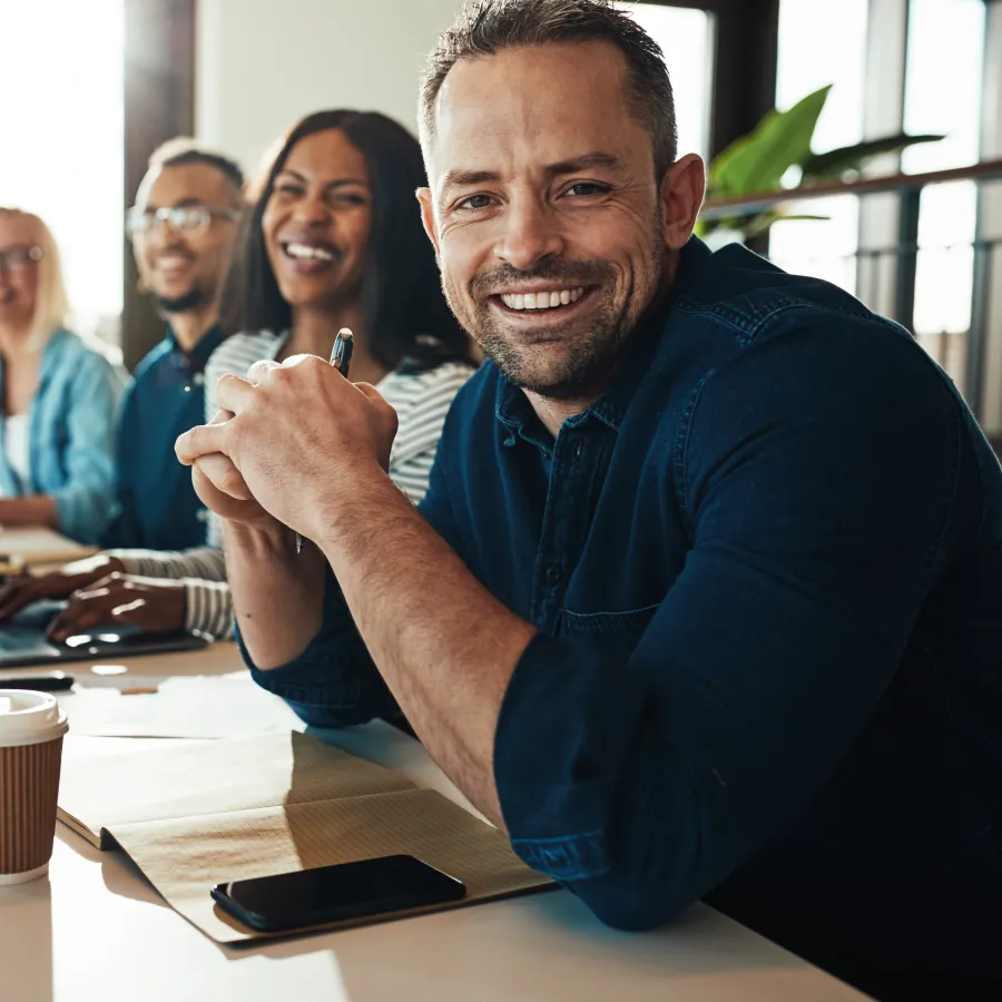 A diverse team collaborates at a table with laptops, notes, and coffee, smiling and engaged.