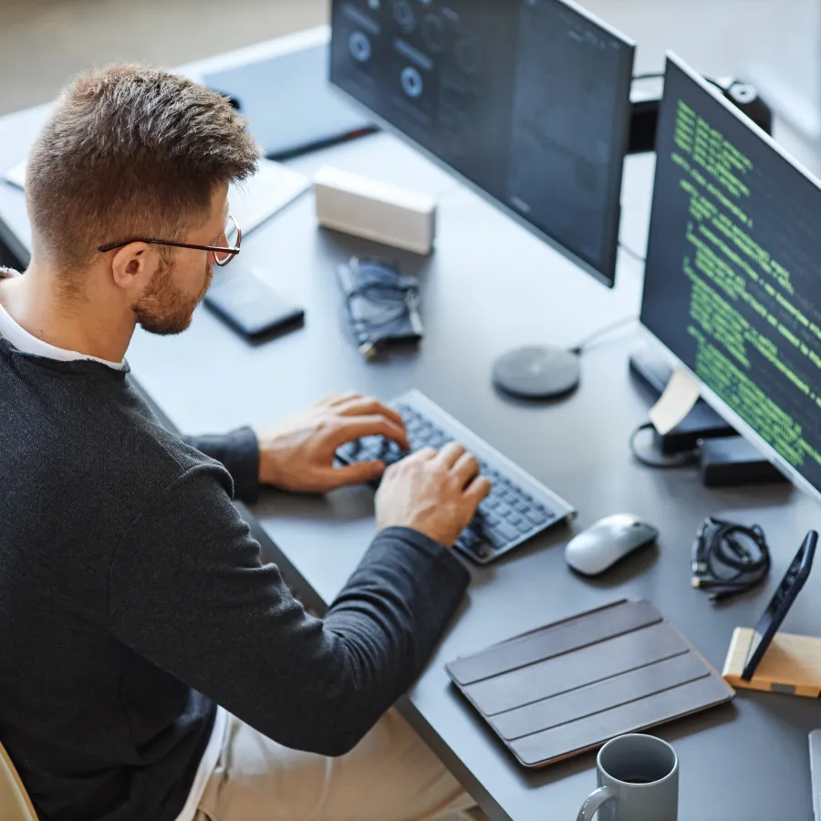 A person coding at a dual-monitor setup with a sleek modern workspace.