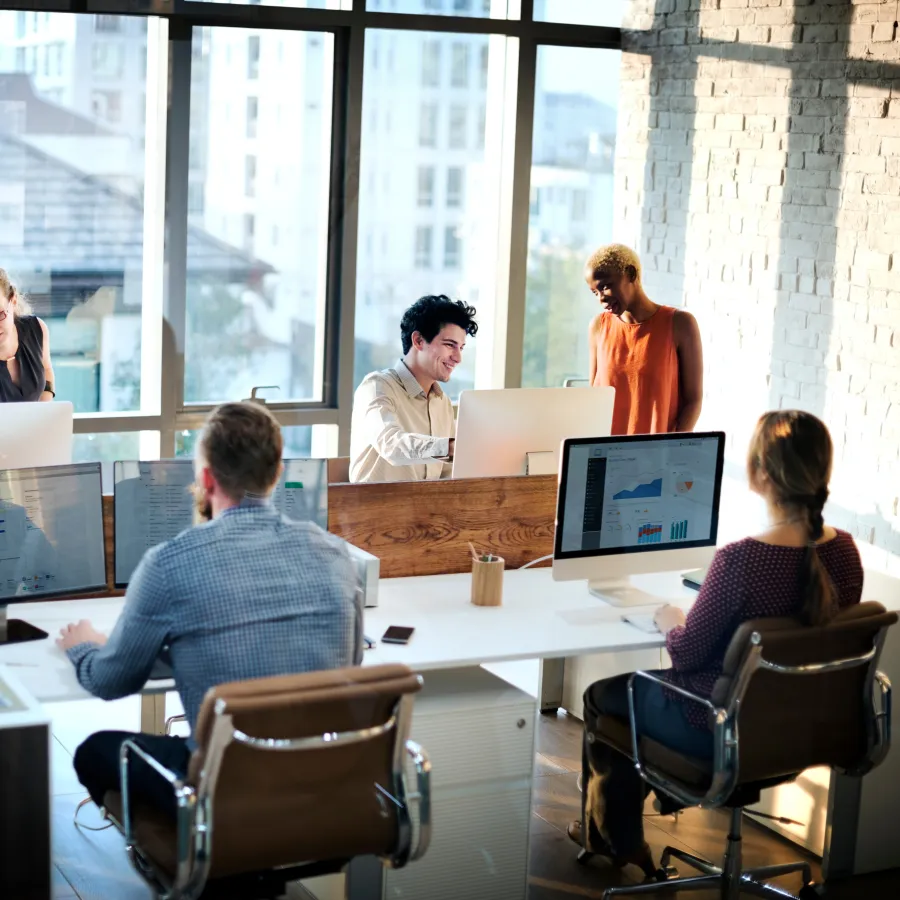 A modern office environment with diverse colleagues collaborating at workstations.