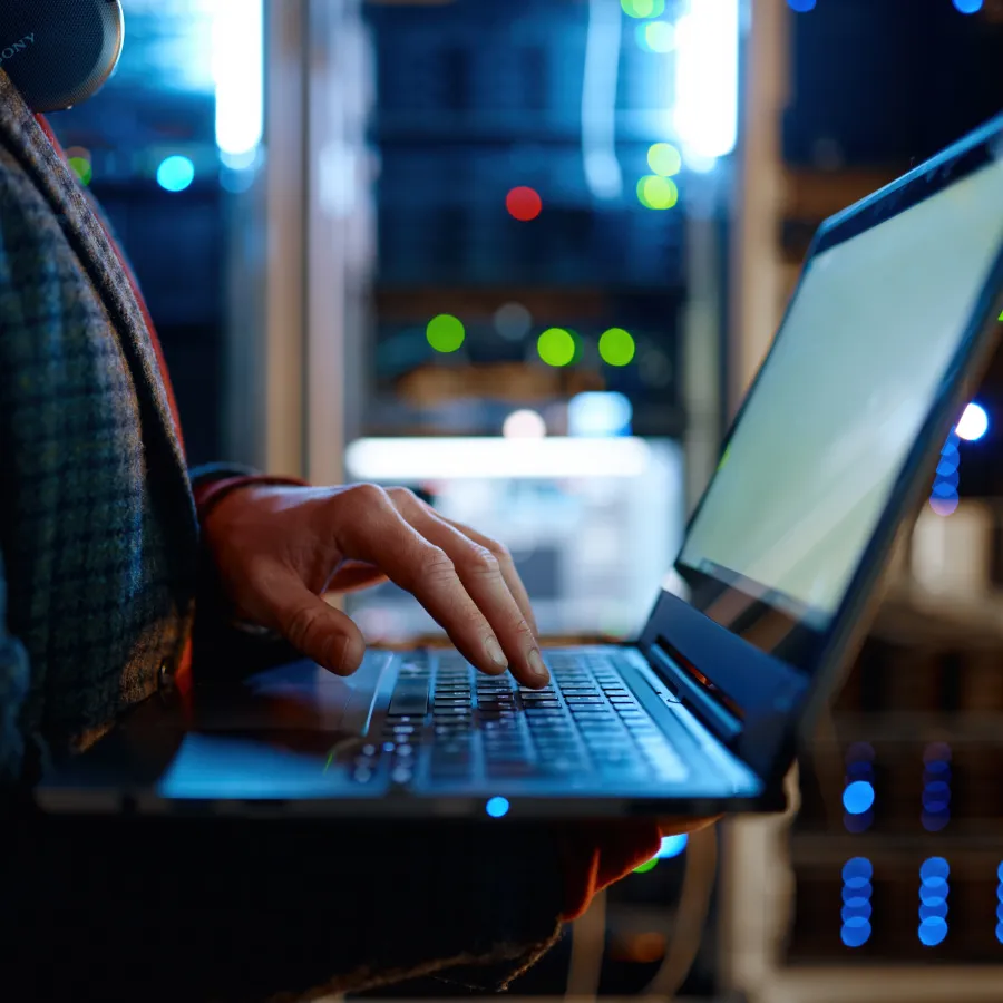 Person using a laptop in a server room with colorful lights in the background.