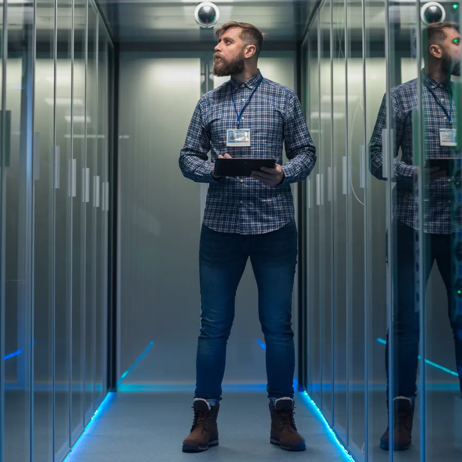 A tech professional holds a tablet in a server room surrounded by reflective glass panels.