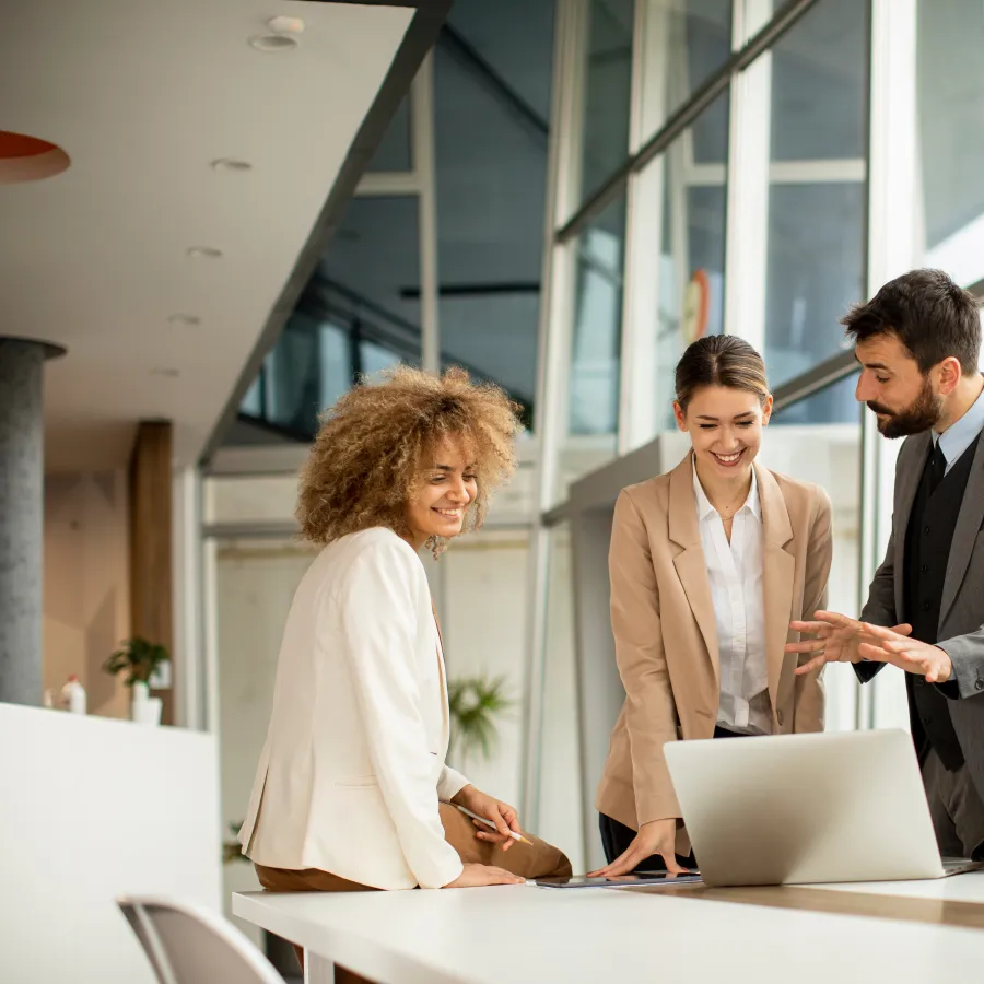 Business team collaborating on a laptop in a modern office setting with large windows.