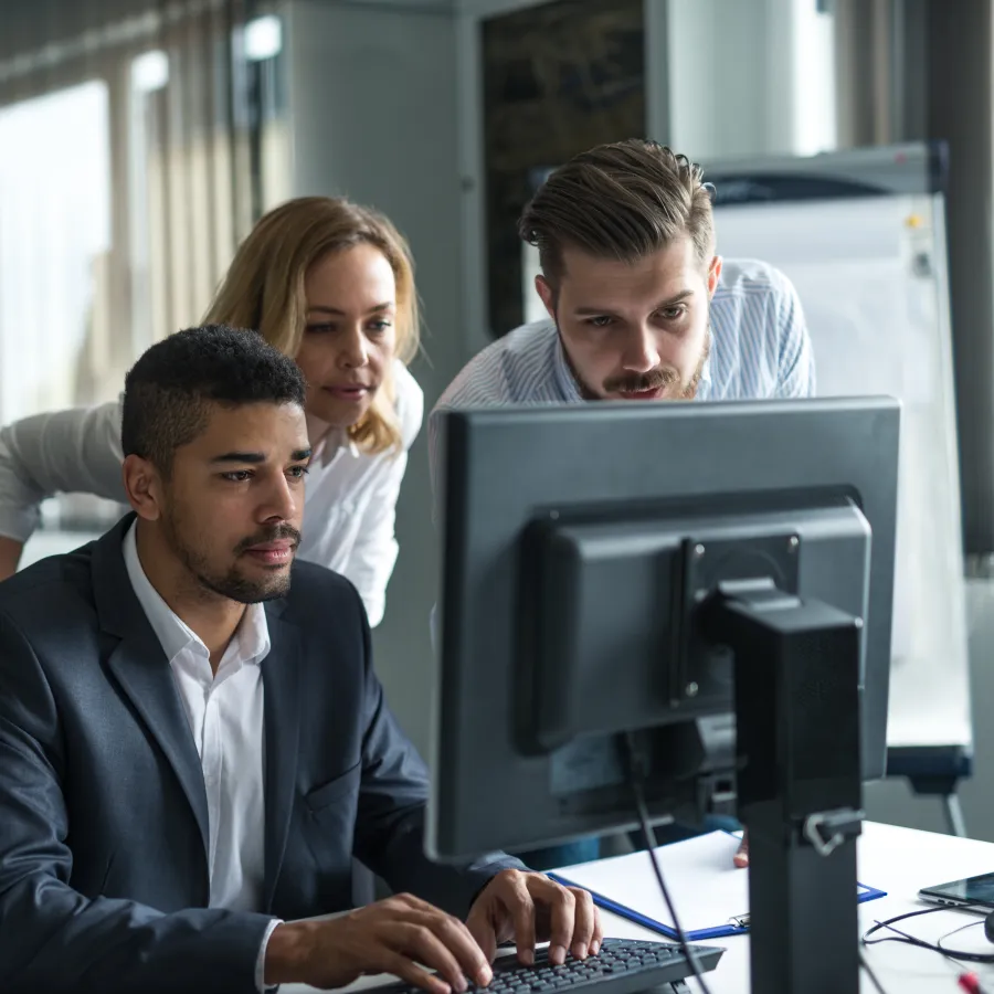 Three colleagues collaborating at a computer in a modern office setting, focused on a project.