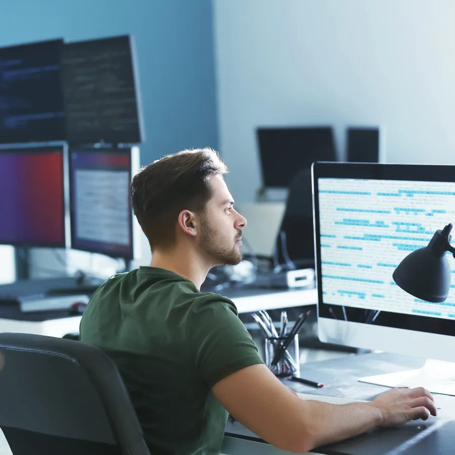 Man working at a dual-monitor workstation in a modern office environment.