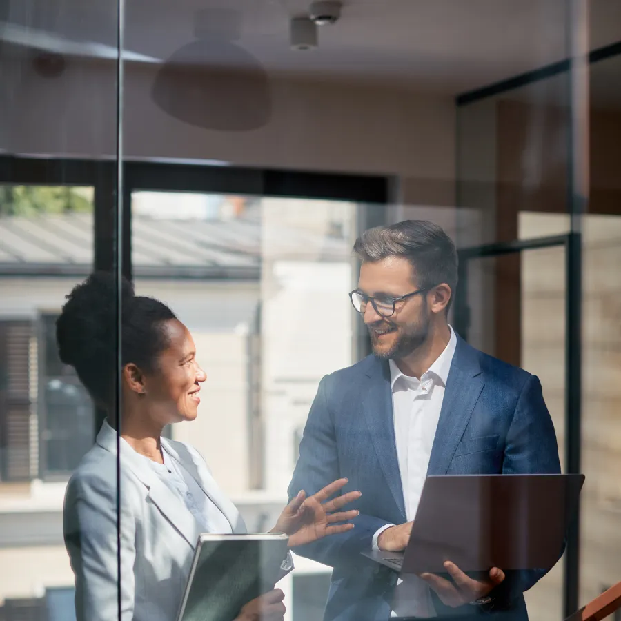 Two professionals discussing in an office space with a laptop and documents, bright and modern environment.