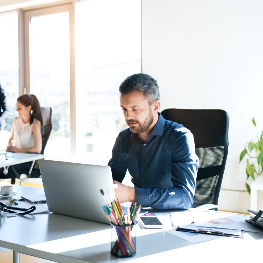 Modern office scene with professionals working on laptops and collaborating in a bright environment.