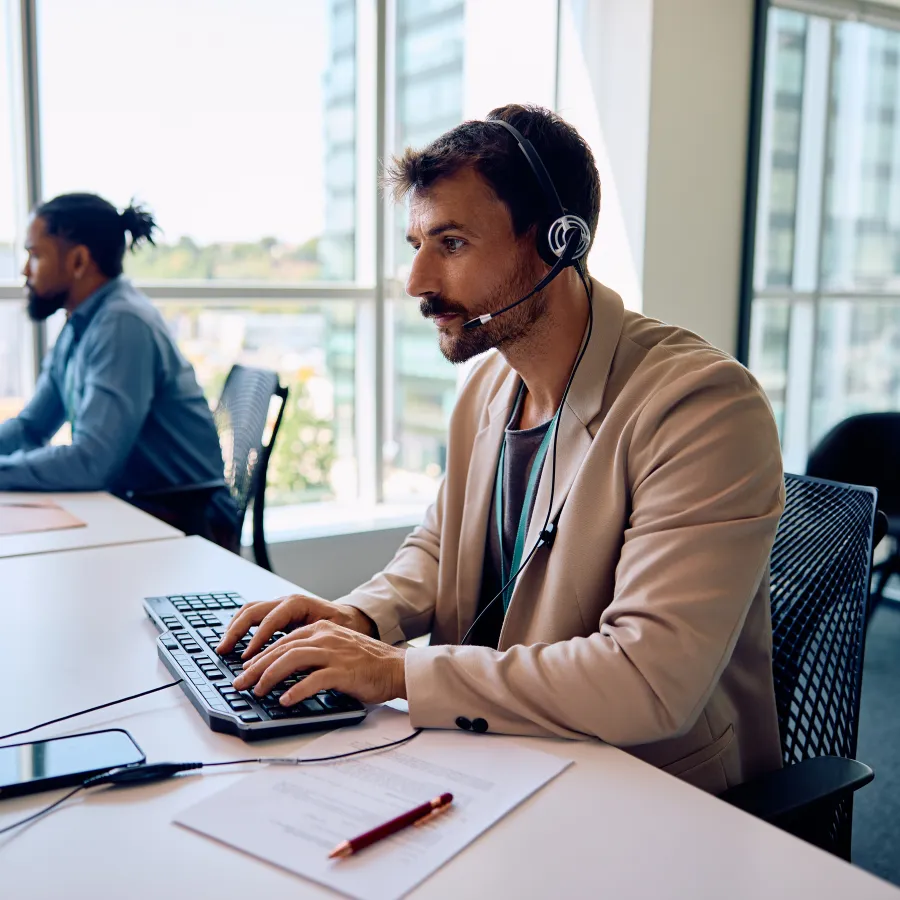 A man with a headset working at a desk with computers in a modern office environment.