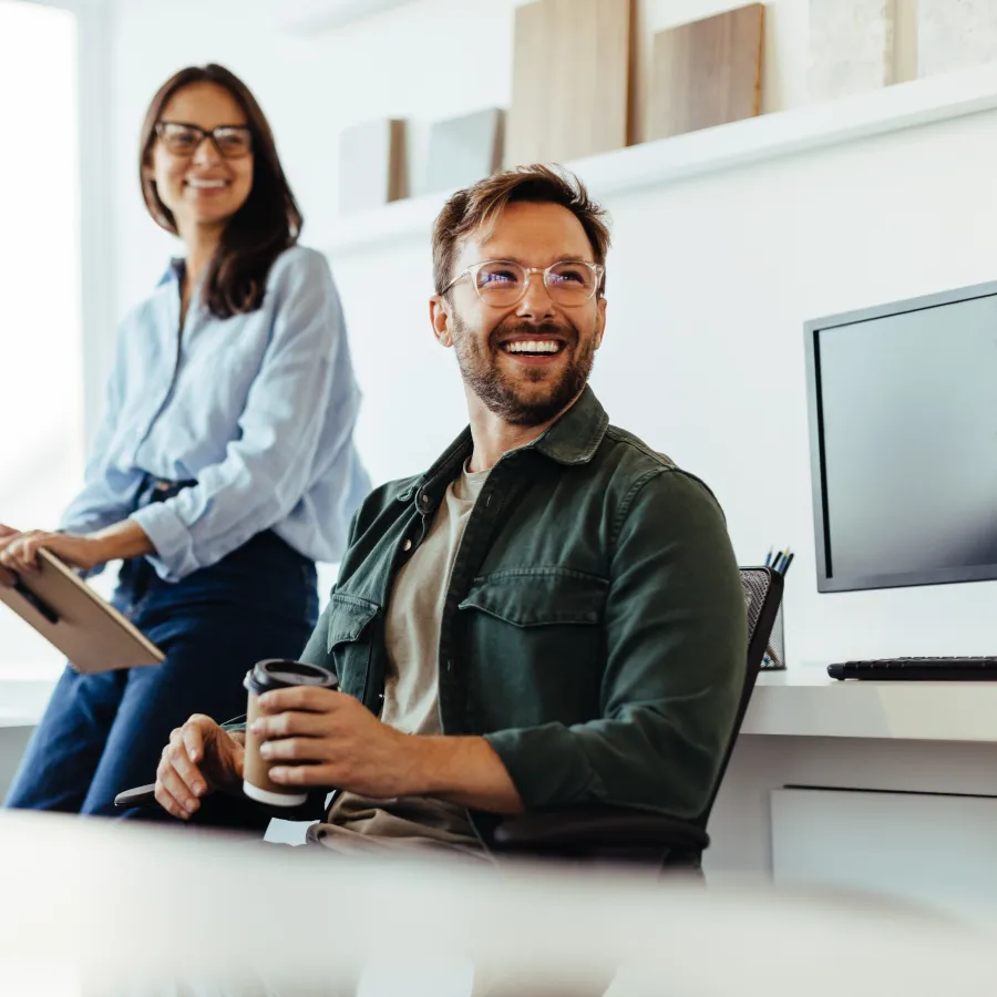 Smiling colleagues in a modern office, engaged in a friendly conversation with casual attire.