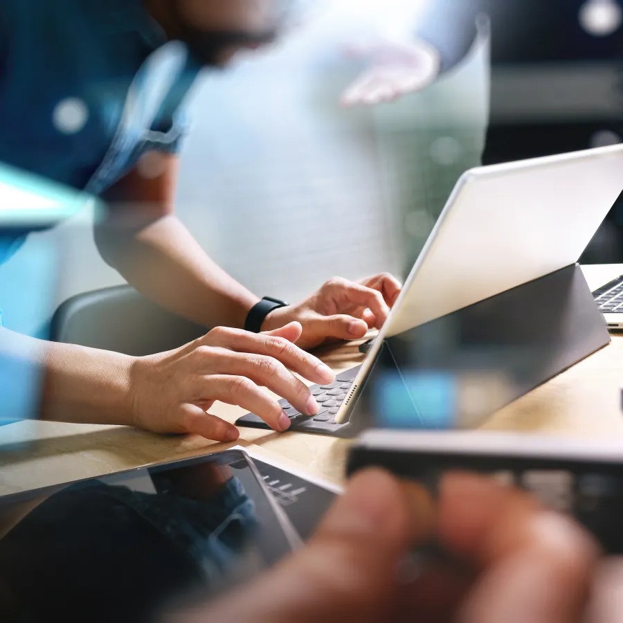 Close-up of hands typing on a laptop during a collaborative work session in an office.
