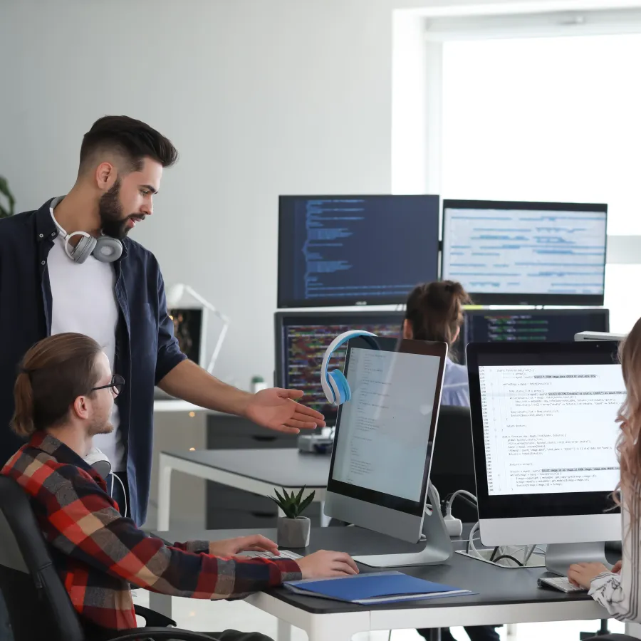 Team of professionals collaborating at modern office workstations with computers and coding on screens.