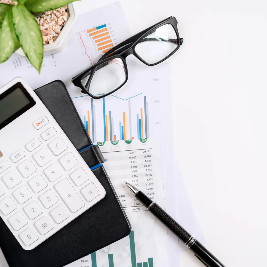 Calculator, glasses, pen, and documents showcasing financial charts and analysis on a white desk.