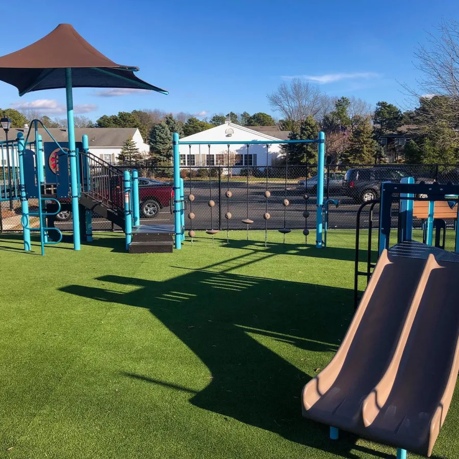 Bright playground featuring slides, climbing structures, and a shaded area on a sunny day.