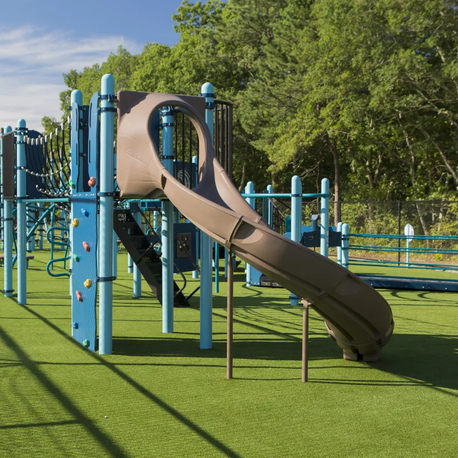 Colorful playground equipment featuring a brown slide on green turf under a clear blue sky.