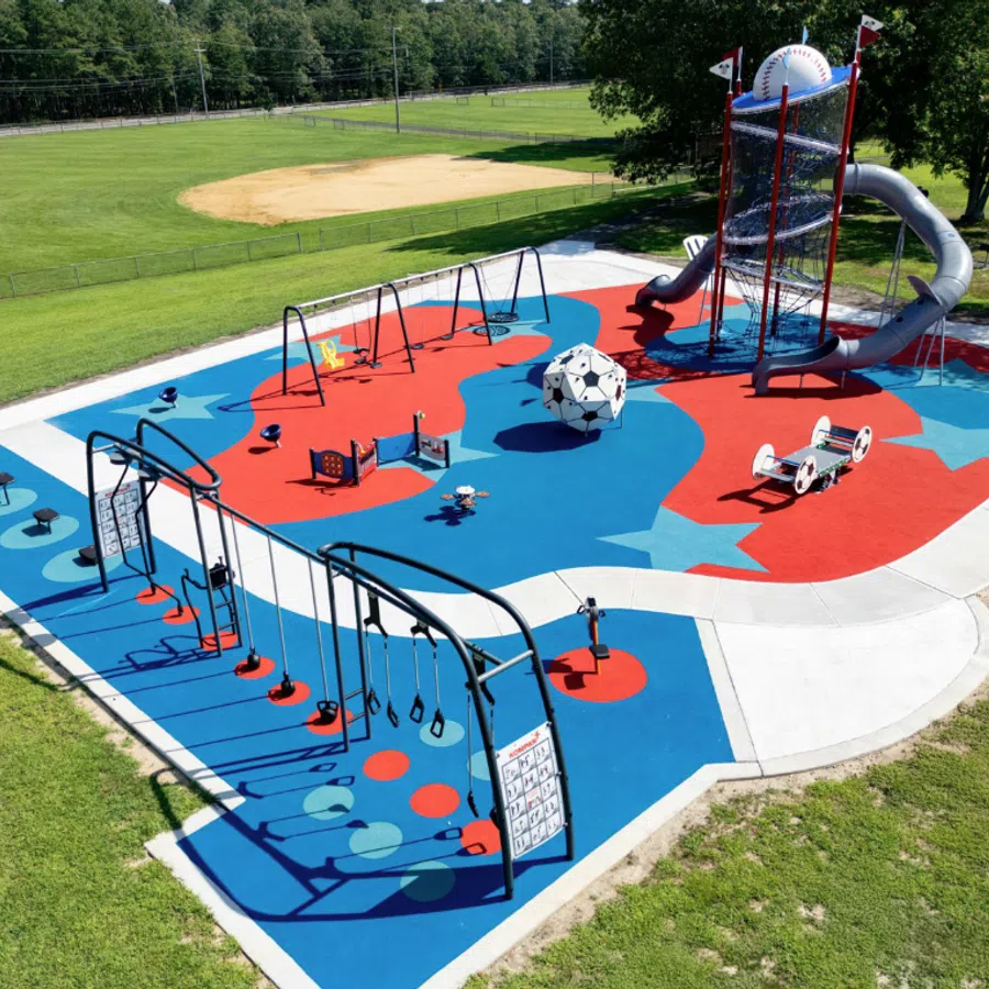 Colorful outdoor playground with swings, slides, climbing structures, and a soccer ball centerpiece on blue and red surface.