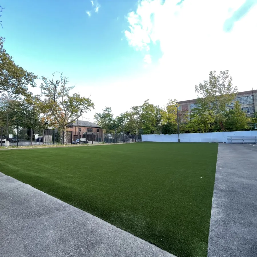 a green lawn with a fence and trees and buildings in the background