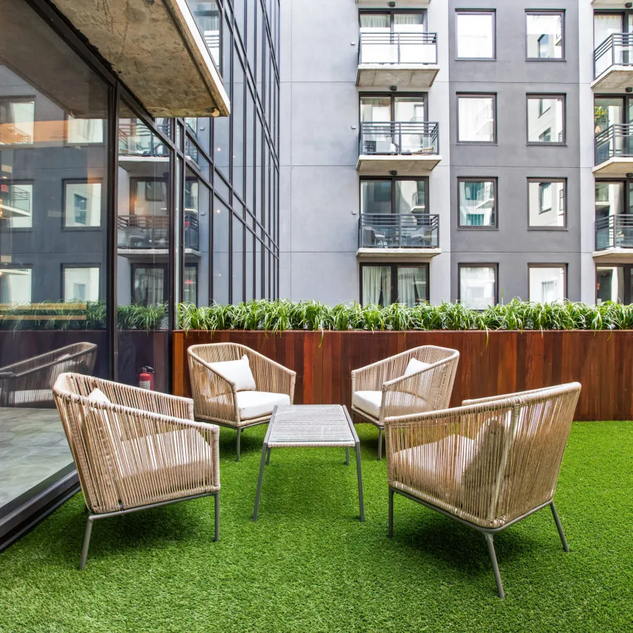 Outdoor seating area with wicker chairs and a table on artificial grass next to modern apartment building