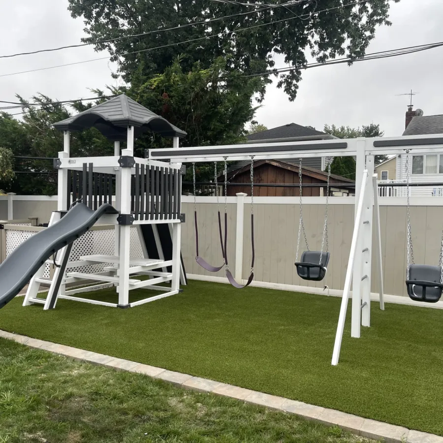 Backyard playground with white and black playset featuring slide, swings, and artificial grass under an overcast sky