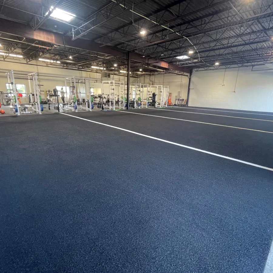 Spacious indoor gym with black rubber flooring, white lane markings, and weightlifting equipment along walls.