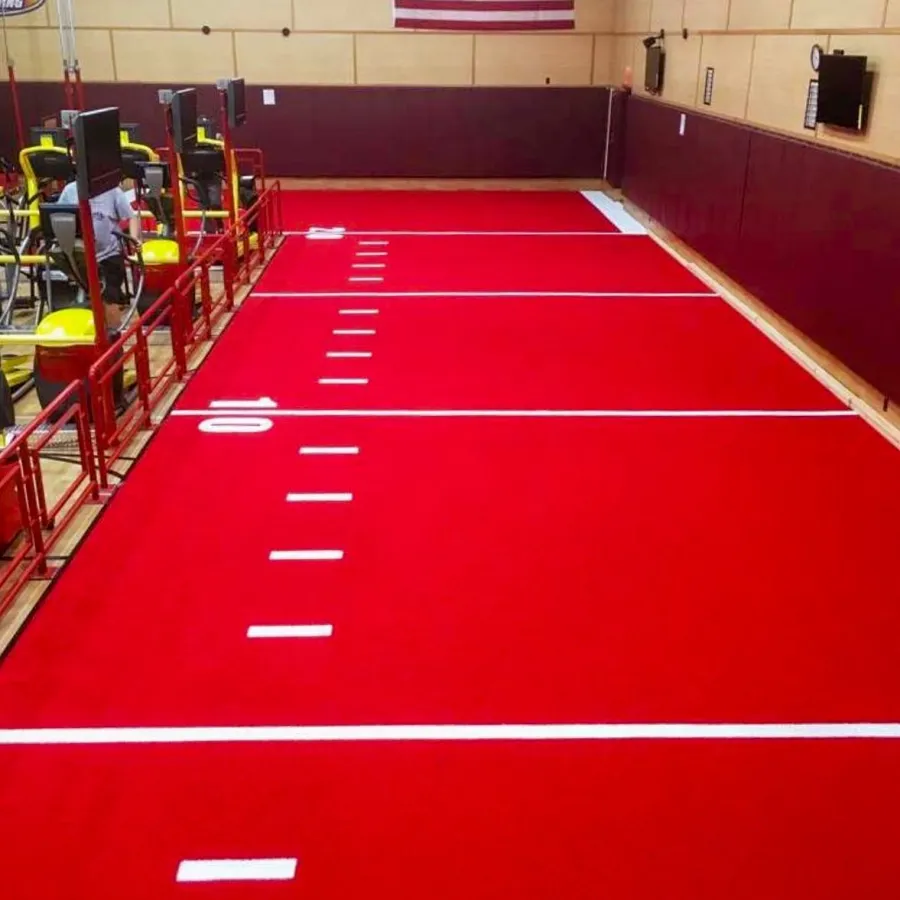 Indoor gym area with bright red artificial turf marked with white yard lines for sports training.
