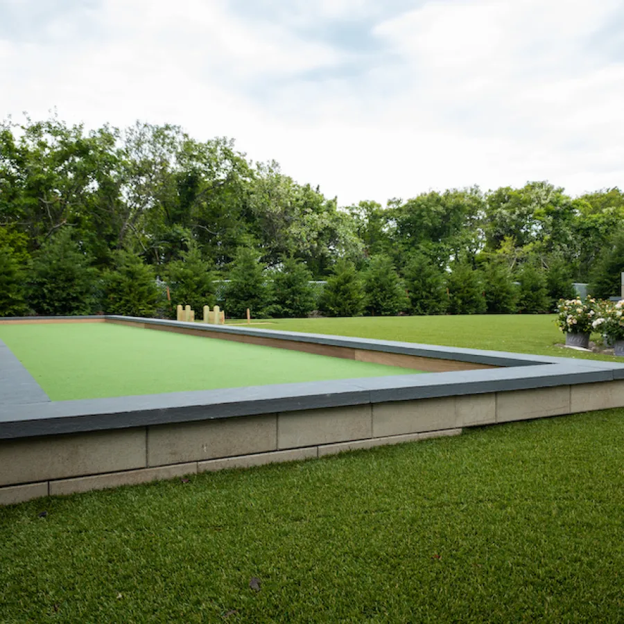 A sleek, modern bocce ball court surrounded by lush greenery and manicured landscaping.
