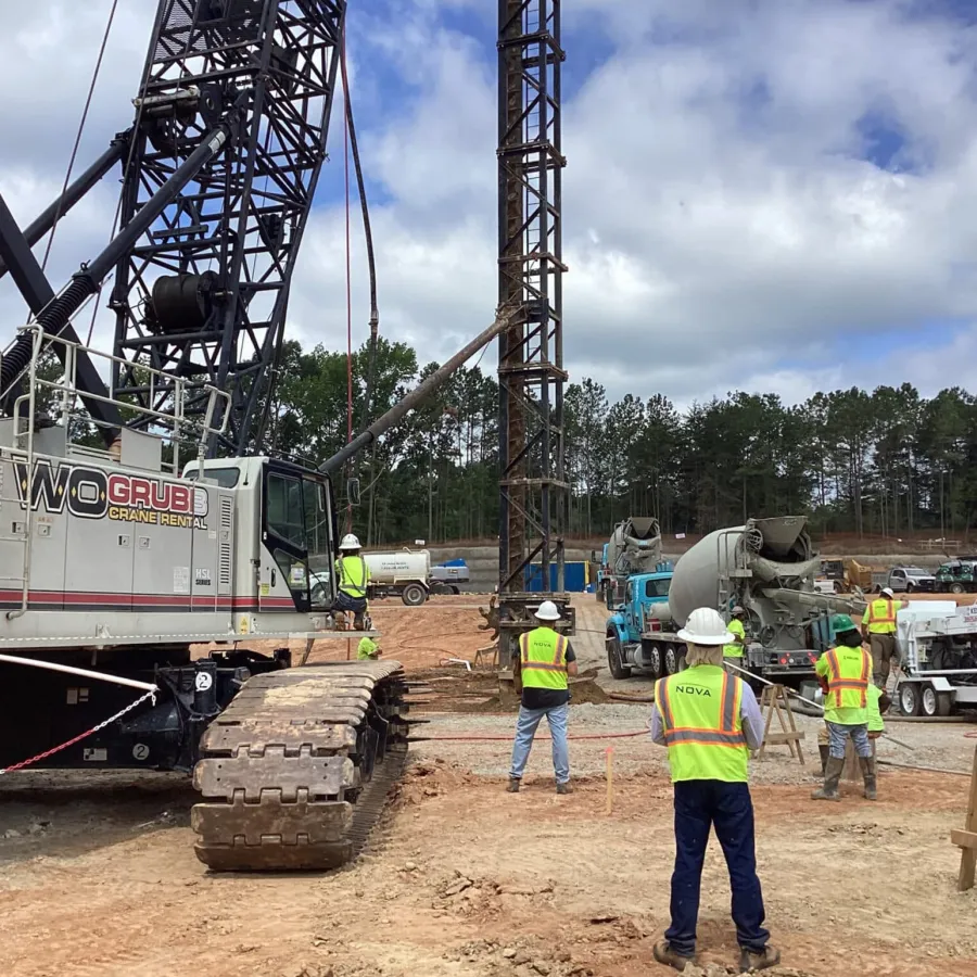 Construction workers in safety vests operating heavy machinery at an outdoor building site under a cloudy sky