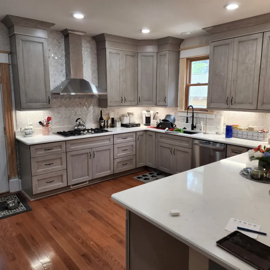 Modern kitchen with gray cabinets, white countertops, stainless steel appliances, and hardwood floors under natural light.