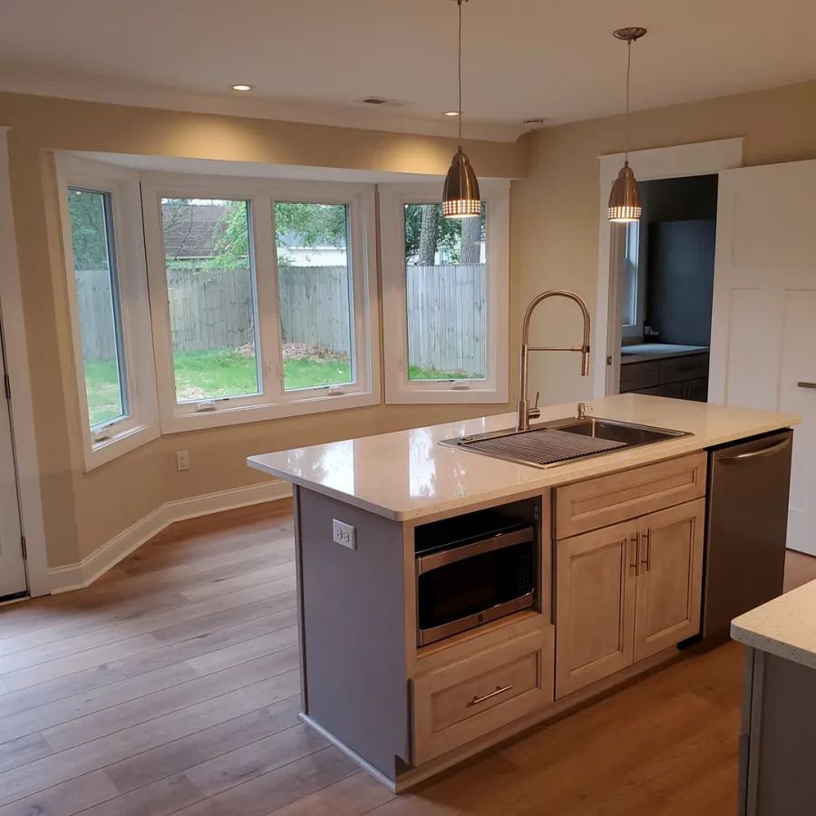 Modern kitchen island with sink, microwave, pendant lights, large windows, and sliding glass door to backyard.