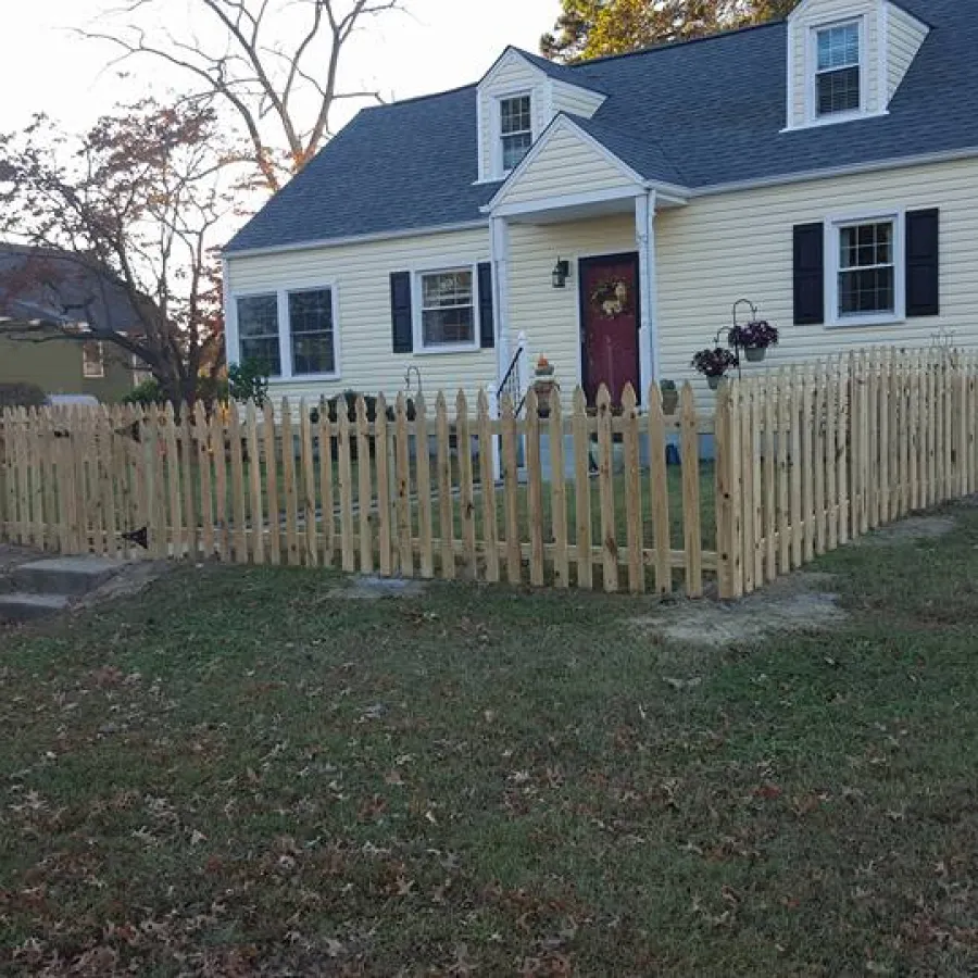 White house with a dark roof surrounded by a newly installed wooden picket fence on a grassy yard.
