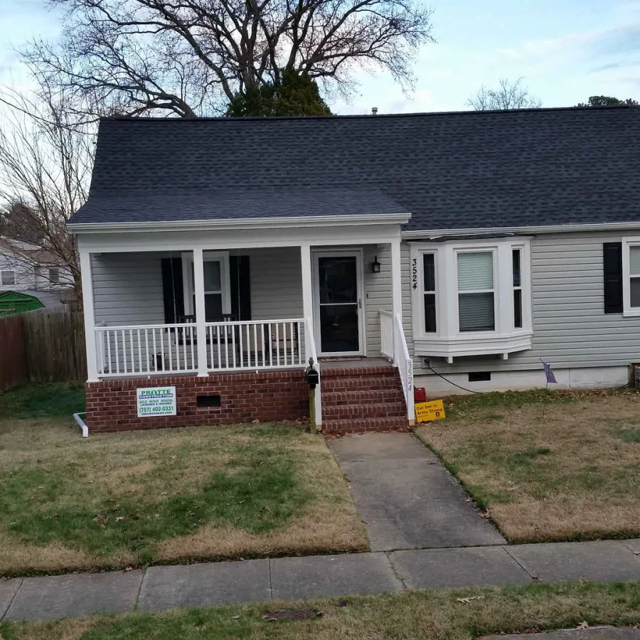 Single-story gray house with a porch, front lawn, sidewalk, and a wooden fence on the left side.