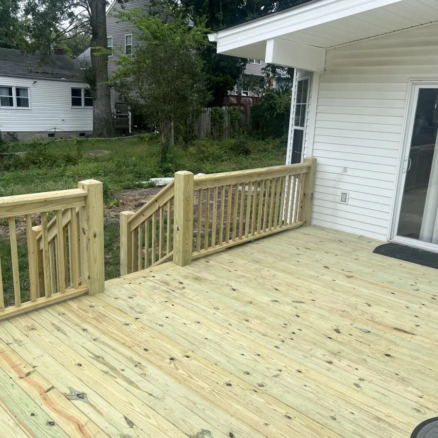 Newly built wooden deck with railings attached to white house overlooking backyard with greenery.