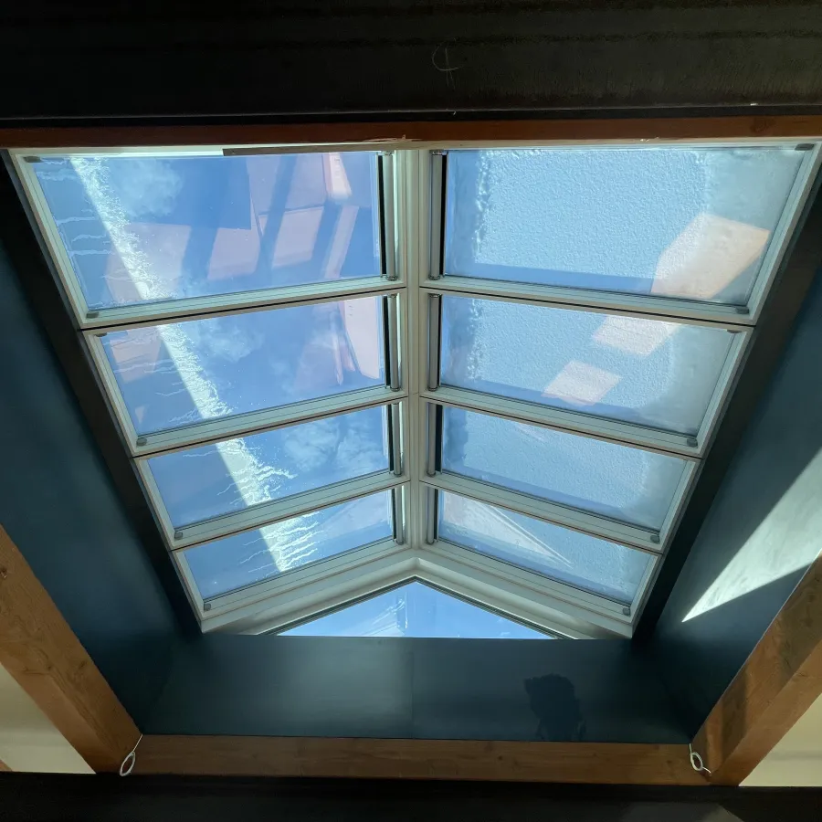 Modern skylight with snow on glass panels and wooden beams framing the ceiling in a cozy room
