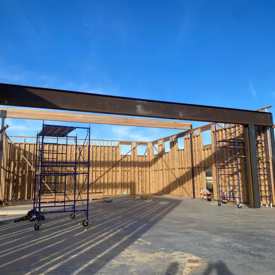 Wooden framed construction site with steel beams and scaffolding under a clear blue sky.