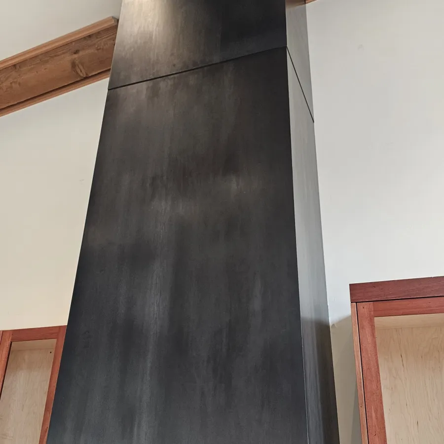 Modern black metal kitchen range hood with wooden cabinets and white walls in a contemporary kitchen.