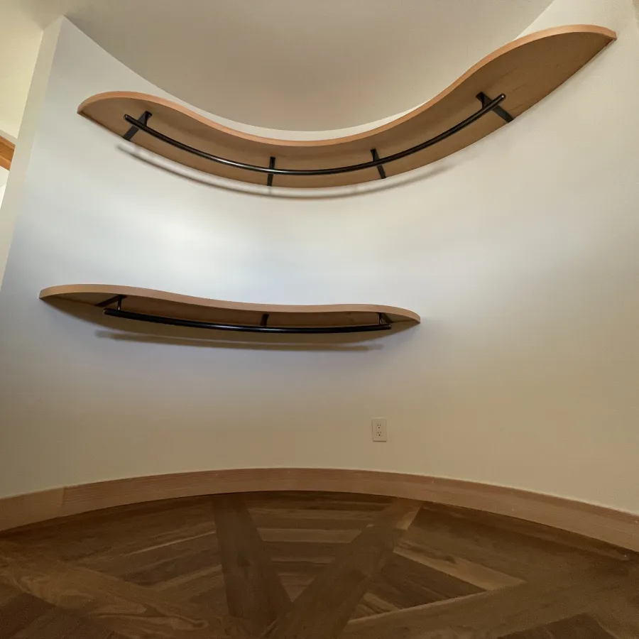 Curved wooden shelves mounted on a white wall above patterned hardwood flooring in a modern interior.