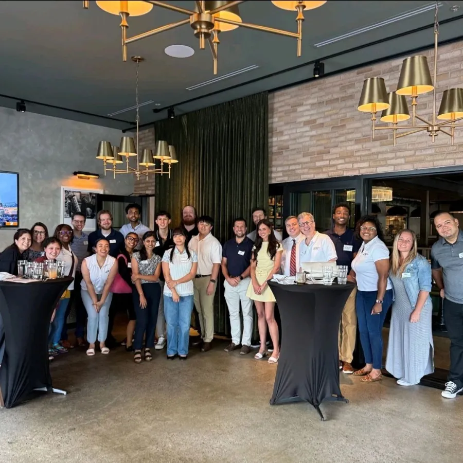 Diverse group of people posing in a modern event space with chandeliers and tall cocktail tables.