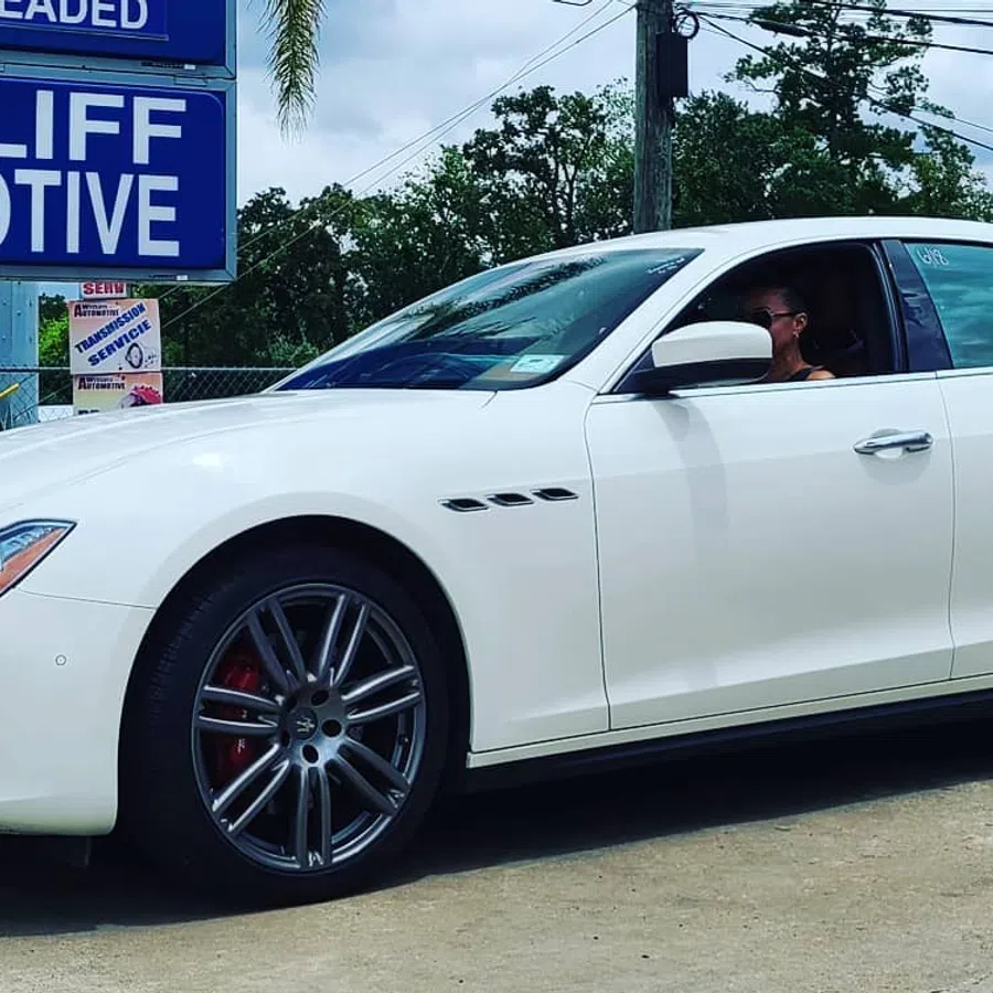 White luxury sedan parked outside Wycliff Automotive service center on a sunny day with visible signage.