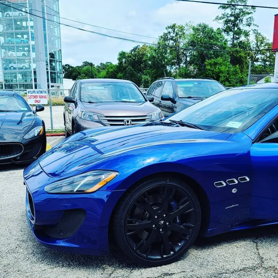Blue and black Maserati sports cars parked outside an automotive repair shop on a sunny day.