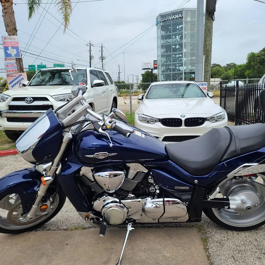 Blue Suzuki Boulevard motorcycle parked next to white Toyota SUV and BMW sedan in urban setting.