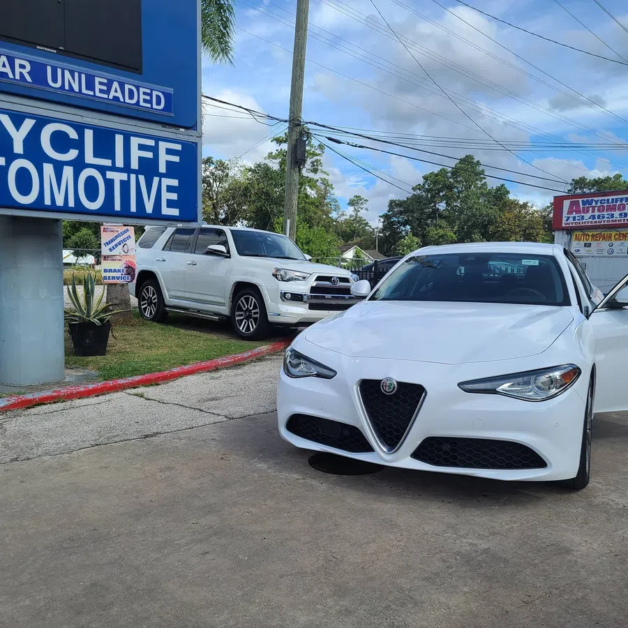 White Alfa Romeo sedan parked at automotive service center with white SUV and service signs in background