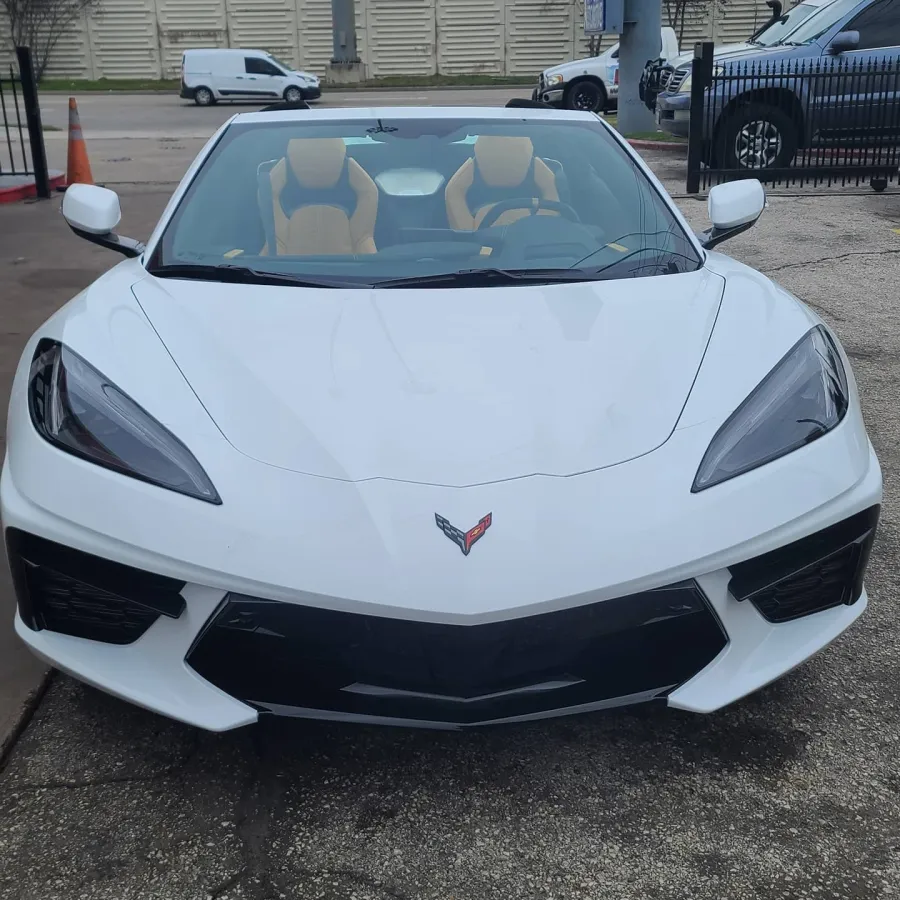 Front view of a white Corvette sports car with tan interior parked on asphalt near traffic cones.