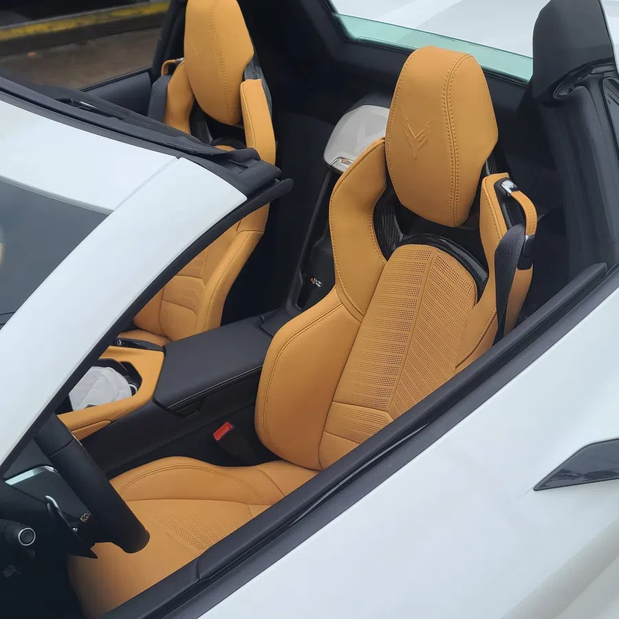 Close-up of tan leather sports car seats inside a white convertible with black interior accents.