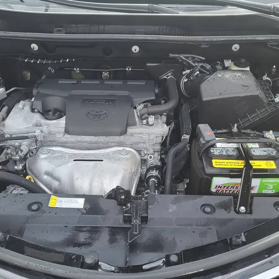 Open hood view of a Toyota car engine bay showing engine, battery, coolant reservoir, and various components.