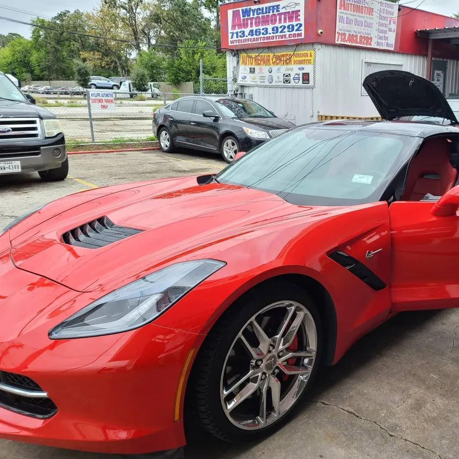 Red sports car with open door parked outside Wycliffe Automotive repair shop with other vehicles nearby.